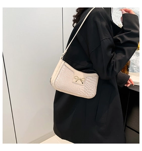 Detail of creamy white croc-effect leather underarm bag with gold bow buckle on a model