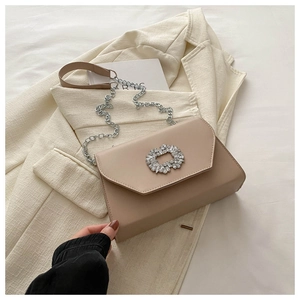 Detail of beige envelope shoulder bag featuring a large rhinestone buckle and silver chain