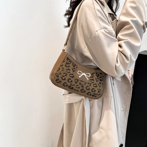 Leopard print shoulder bag with golden bow accent shown on model in beige trench coat