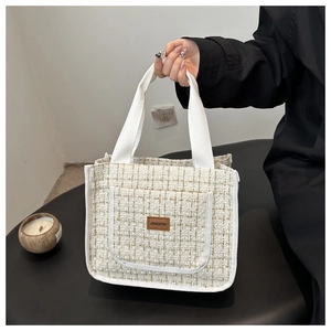 Detail of cream woven tweed tote bag with gold grid lines and a brown leather logo patch