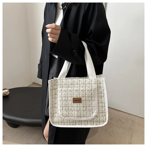 Detail of tweed tote bag showing beige texture and branded leather patch detail