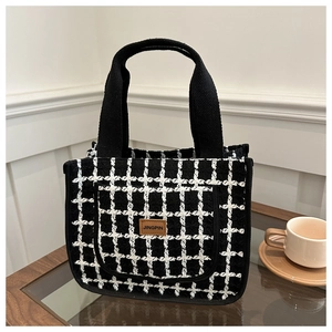 Detail of black and white checkered tweed tote bag with leather label on coffee table