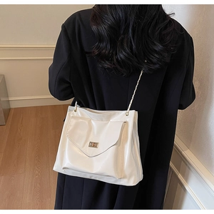 Detail showing creamy white faux leather tote bag with gold chain strap and square metal lock