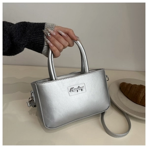 Detail of silver faux leather crossbody bag with metal logo and sleek top handles