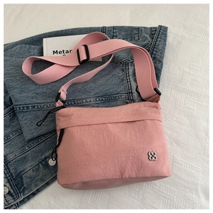 Pink nylon crossbody bag with silver clover logo and adjustable wide strap on white bedding
