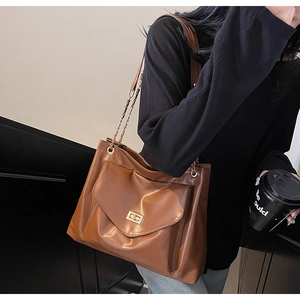 Detailed view of the brown leather shoulder bag featuring a gold chain strap and a turn-lock pocket