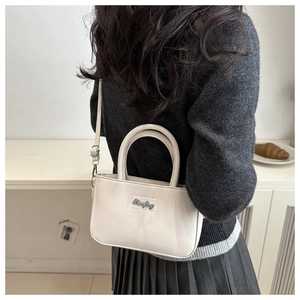 Detail of a creamy white PU leather crossbody bag with a slim strap and metal magnetic clasp
