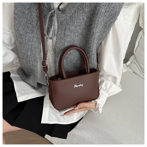 Detail of dark brown PU leather crossbody bag with metal logo and sleek top handle