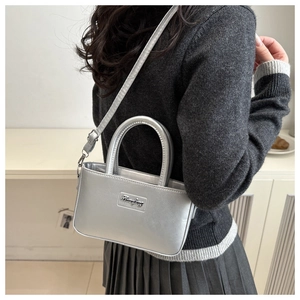 Detail of silver metallic crossbody bag with adjustable strap and top handle on model