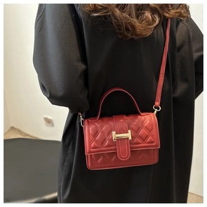 Dettaglio borsa a tracolla trapuntata rossa con fibbia dorata su cappotto nero