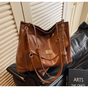 Detail of caramel leather tote bag with gold chain strap and turn-lock pocket on sofa