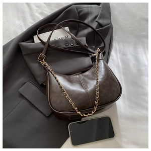 Dettaglio borsa hobo retrò caffè scuro con catena dorata su letto bianco