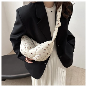 Détail du sac matelassé à fleurs avec large bandoulière porté sur un blazer noir