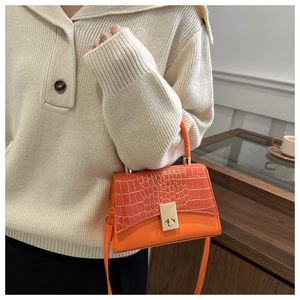Detail of bright orange crossbody bag featuring crocodile embossed leather and gold clasp