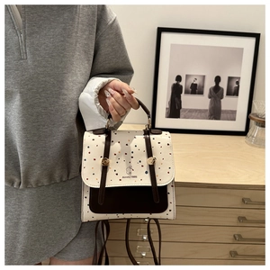 Polka dot backpack with vintage straps and logo detail held in a cozy home setting