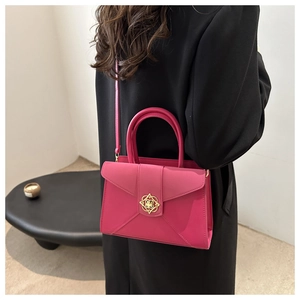 Detail of fuchsia envelope handbag featuring a geometric gold clasp and top handle