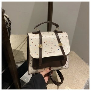 Close-up of beige polka dot backpack featuring brown leather flap and rabbit logo detail