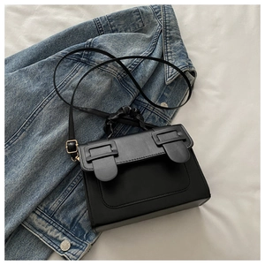 Detail of black pleated handle handbag and decorative buckles on blue denim jacket