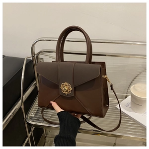 Detail of a brown leather patchwork handbag with a golden circular clasp and strap