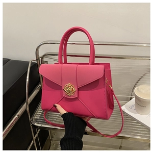 Detail of magenta structured handbag featuring a gold petal-shaped metal buckle and smooth finish