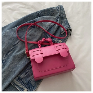 Detail of a pink textured faux leather handbag featuring a ruched handle and metal buckles
