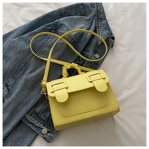 Detail of lemon yellow pleated handle and decorative flap closures on small square bag