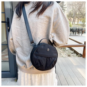 Close-up of a black nylon round crossbody bag featuring a metallic M logo and leather strap