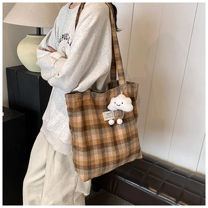 Detail of checkered canvas tote bag with a white plush cloud charm and brown plaid texture