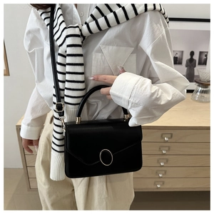 Détail d'un sac bandoulière en cuir noir avec une boucle ronde en métal doré sur le rabat