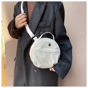 Model wearing round cream nylon crossbody bag on a black wool coat, casual minimalist style