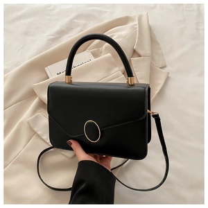 Détail d'un sac bandoulière en cuir noir avec fermoir métallique doré ovale et poignée