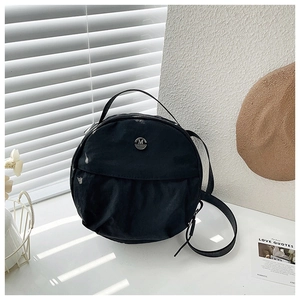 Close-up of black nylon round bag featuring a silver metal M logo and adjustable strap