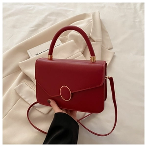 Détail du sac bandoulière en cuir rouge avec boucle dorée ovale et poignée en métal