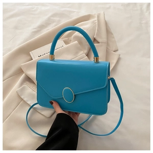 Détail d'un sac bandoulière bleu avec boucle dorée et poignée ronde sur tissu doux