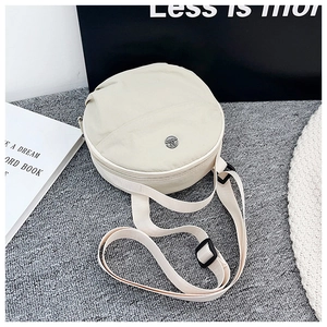 Detailed close-up of a cream nylon round crossbody bag with adjustable strap and metal logo