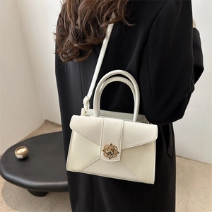 Minimalist cream white crossbody bag with elegant gold filigree clasp on black coat
