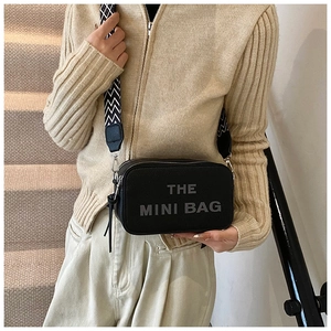 Detail of black leather camera bag with wide geometric strap and printed text lettering