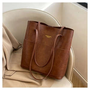 Brown leather tote bag on beige chair featuring spacious design and long shoulder straps