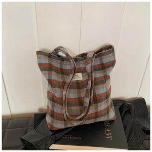 Detail of wool plaid tote bag with logo patch showing brown and blue checkered texture