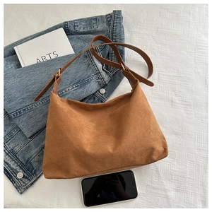 Flat lay of caramel suede tote bag with leather strap and accessories on white background