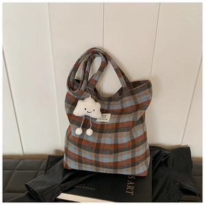 Detail of plaid canvas tote with a cute plush cloud charm on black leather background