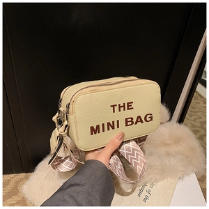 Detail of beige litchi grain camera bag with brown THE MINI BAG text and jacquard strap