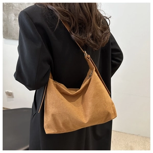 Close-up of brown suede hobo bag with adjustable strap worn with a black blazer