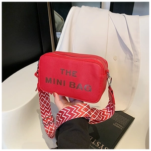 Close-up of red pebbled leather mini camera bag with wide geometric pattern strap