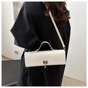 Dettaglio borsa baguette bianca con motivo a coccodrillo e chiusura dorata su cappotto nero