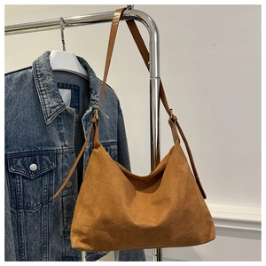 Close-up of brown suede hobo bag hanging on a metal rack with denim jacket background