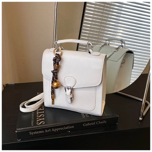 Detail of white square handbag with buckle decor and woven bell pendant on art books