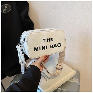 Detail of white lychee leather camera bag with The Mini Bag text and woven strap