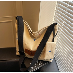 Detail of canvas tote bag featuring colorful letter embroidery and brown leather logo patch