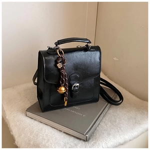 Detail of a vintage black square bag with a flap buckle and a woven bell pendant